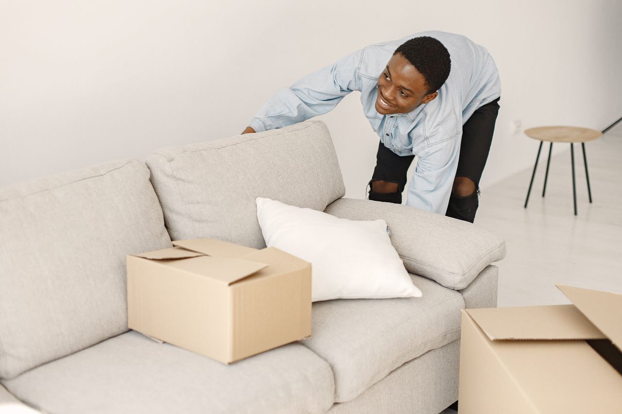 A young man smiles as he organizes cardboard boxes in a modern living room.